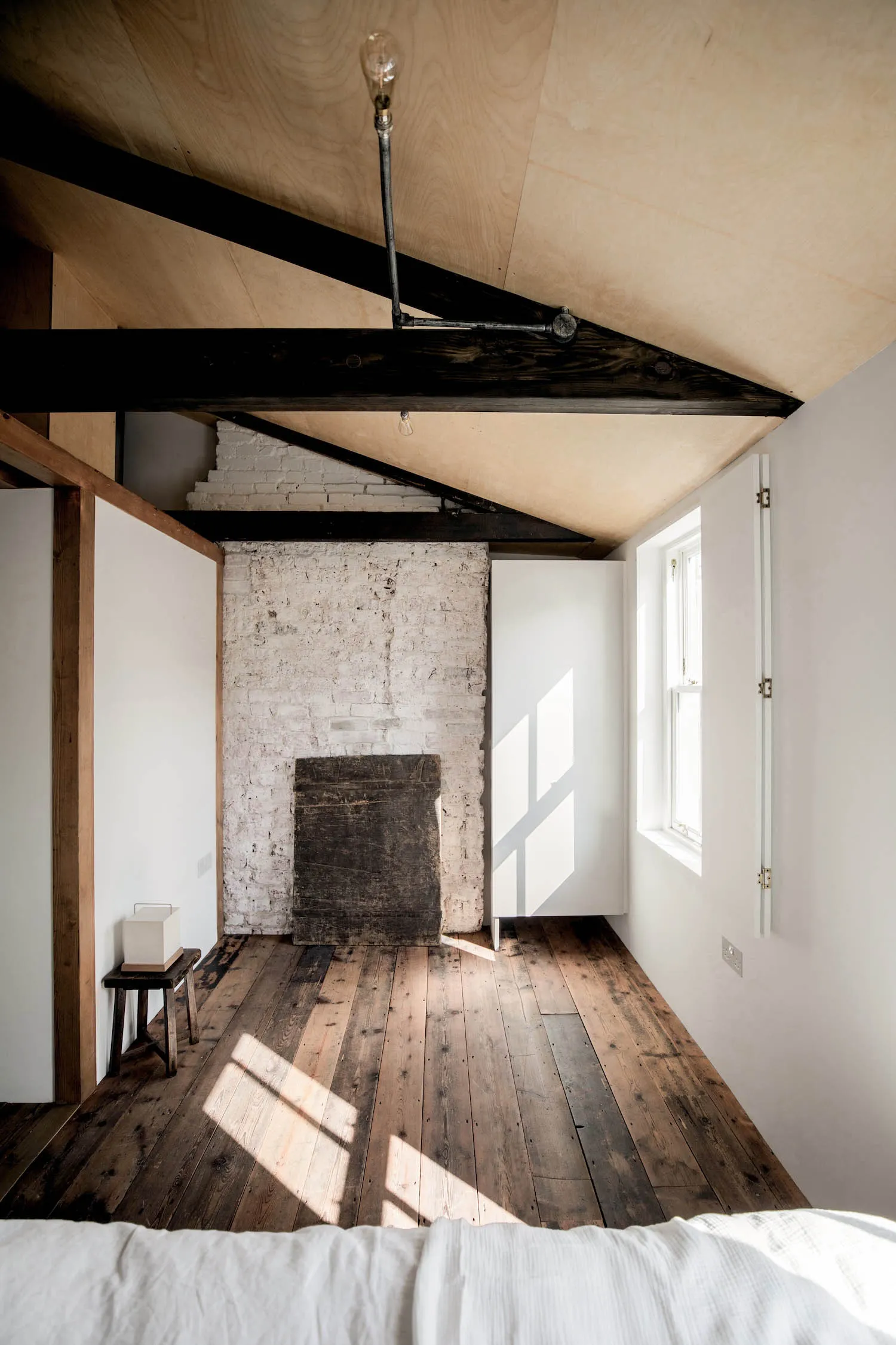 A minimalist bedroom with an angular ceiling, white brick wall, and wooden floor.