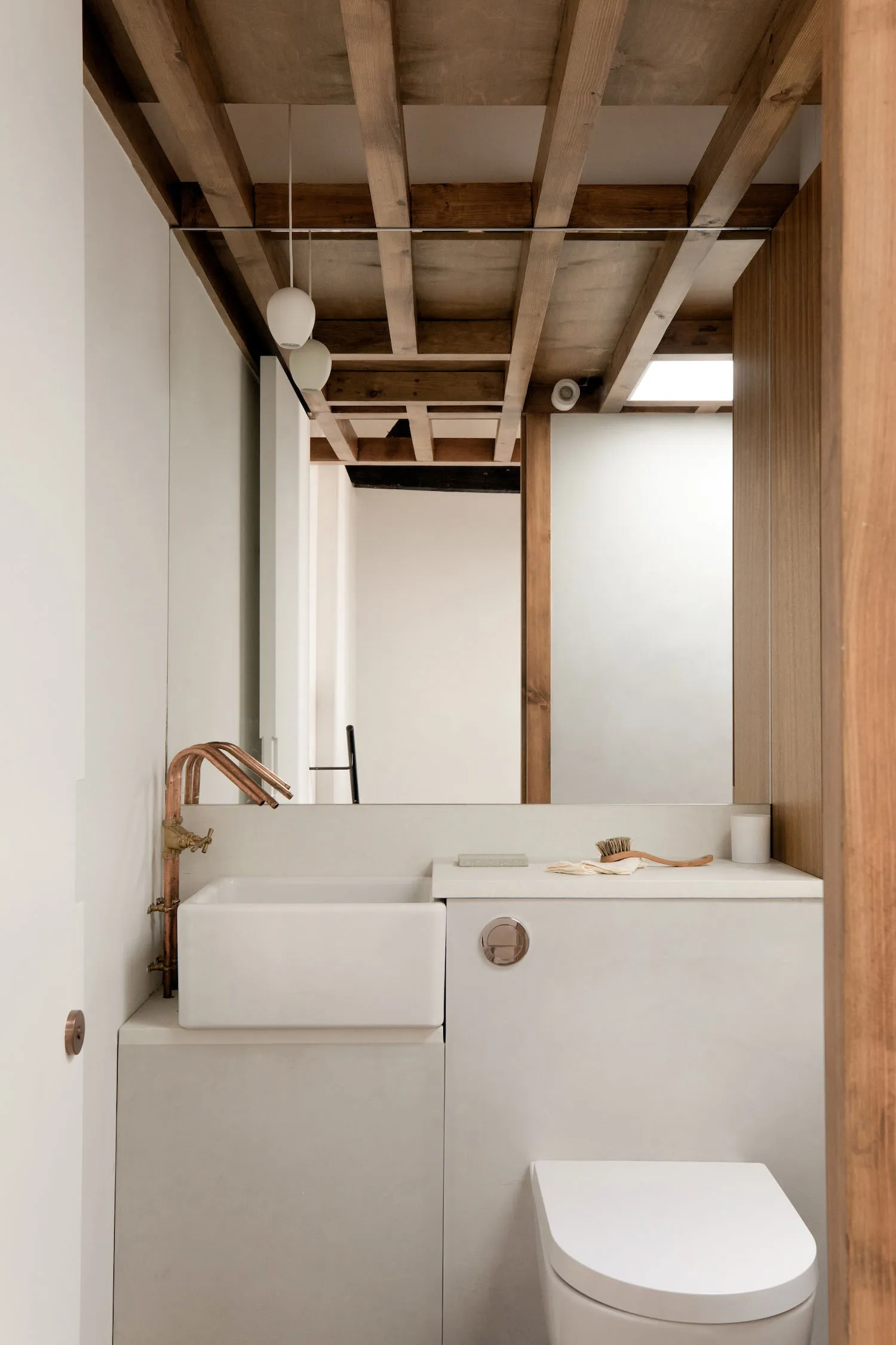 A minimalist bathroom with concrete walls and floor, featuring a white sink, a white toilet, and a mirror.