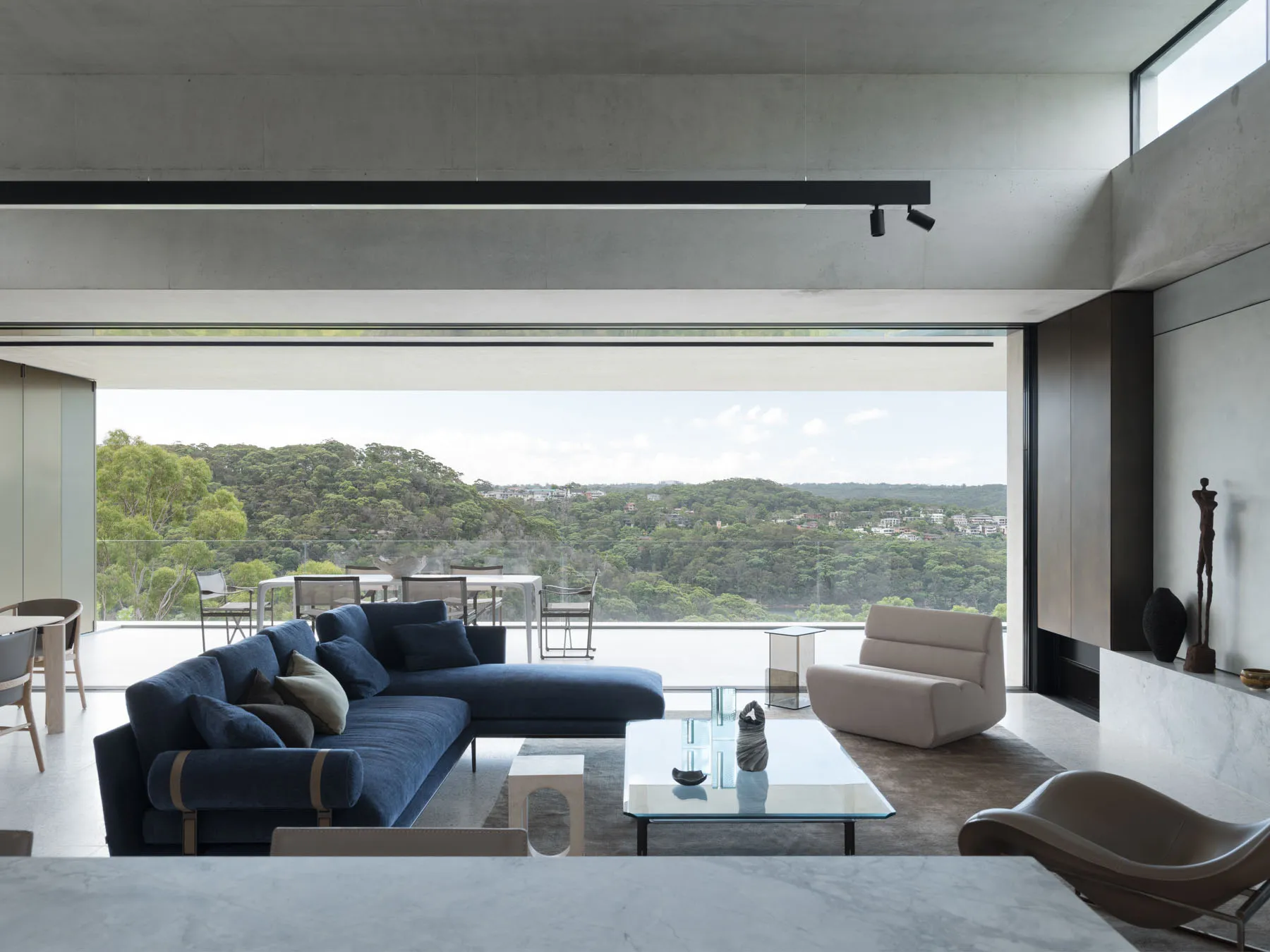 Modern living room with concrete walls and floors, featuring a spacious blue sofa and a glass coffee table.