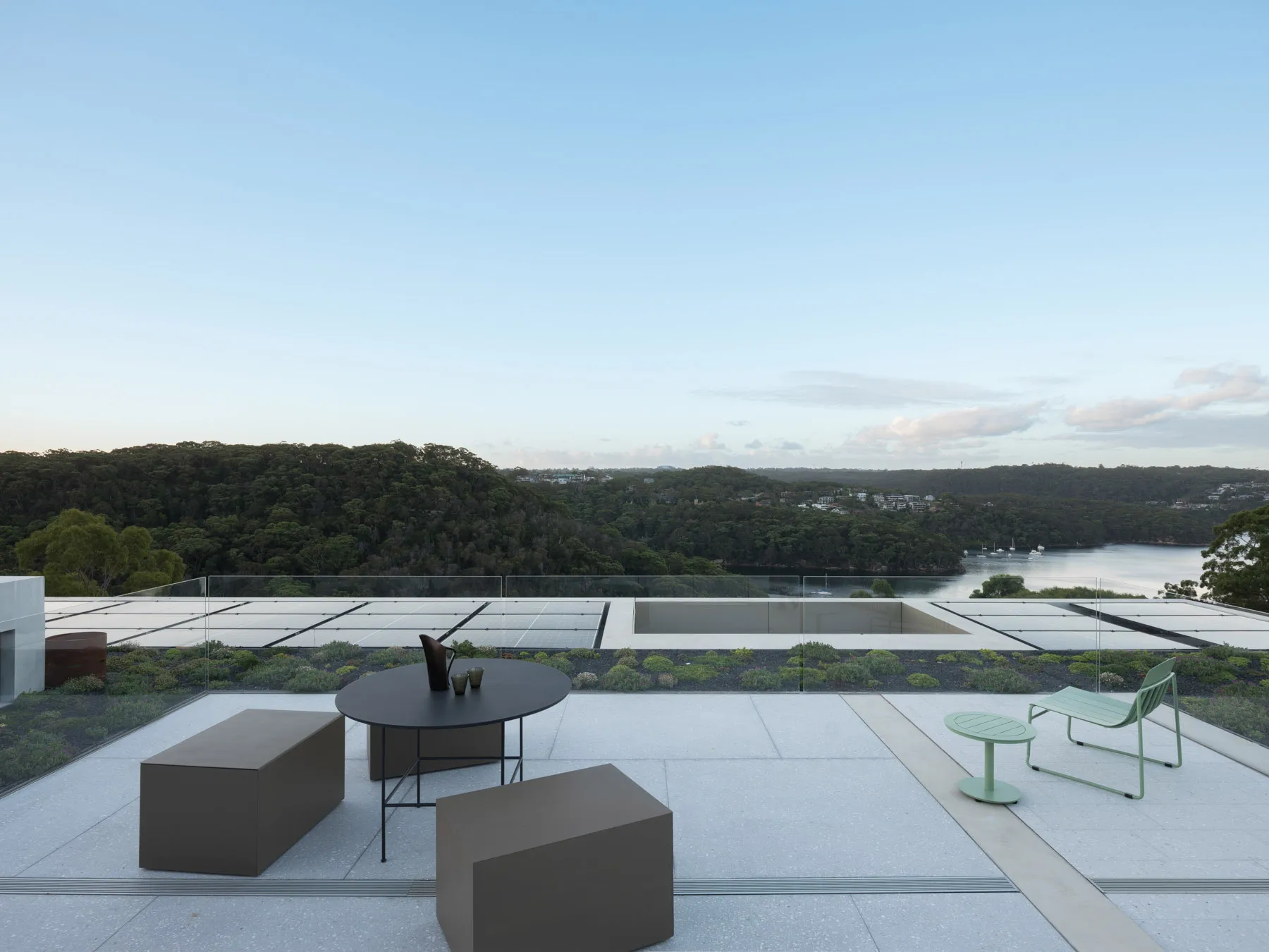 A modern rooftop terrace featuring glass railings, concrete floor, and a view of the blue sky.