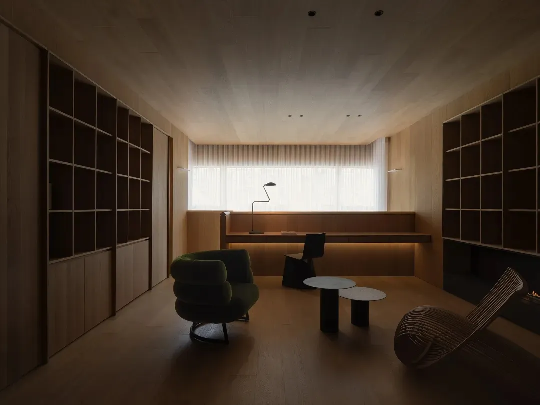 A modern minimalist living room with wooden furniture and flooring, featuring a green armchair, a black chair, and two coffee