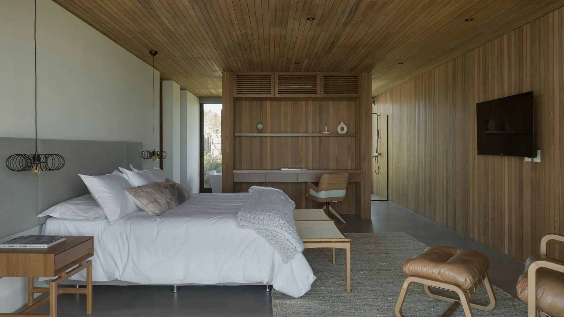 A modern monochromatic bedroom featuring white bedding and a wooden floor with a large bed, wooden shelves, and a wooden chai