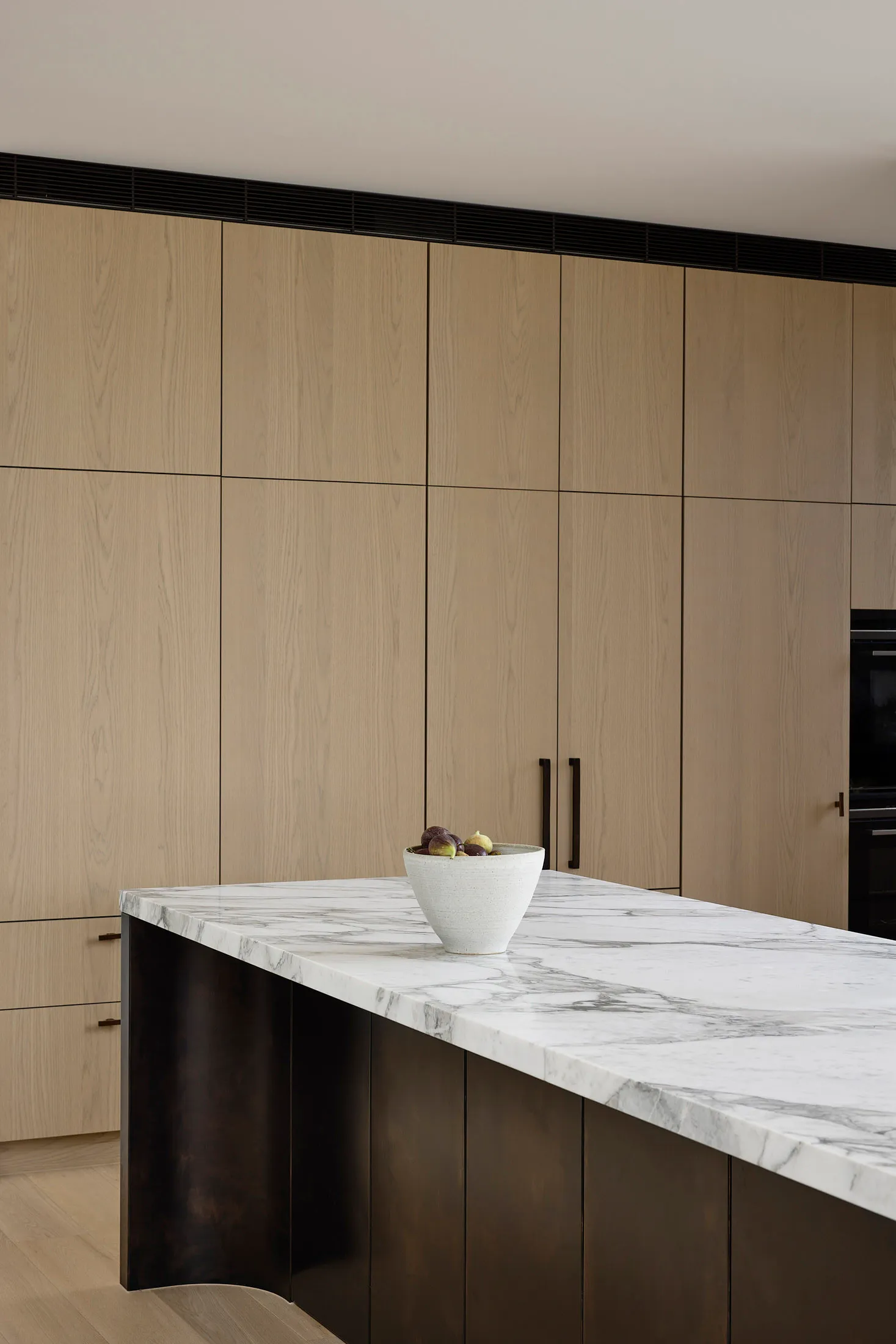 A modern minimalist kitchen featuring a marble countertop with a bowl of fresh figs.