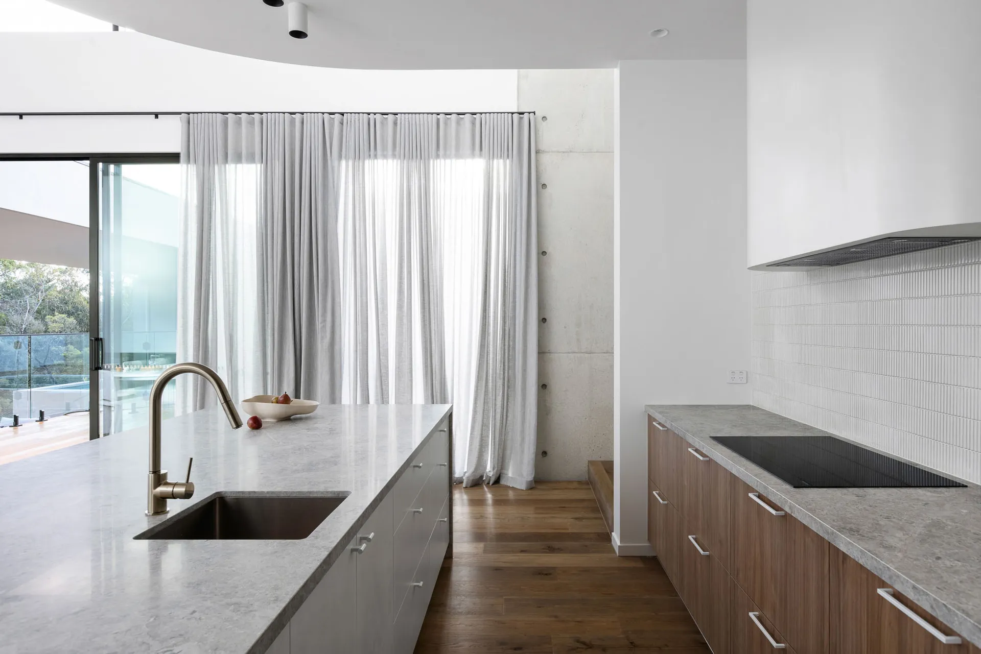 Modern kitchen featuring white countertops, grey cabinets, and large windows with sheer curtains.