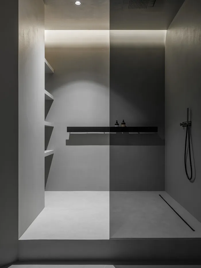 A minimalist shower area with concrete walls and floor, featuring a black and white color scheme and ambient lighting.