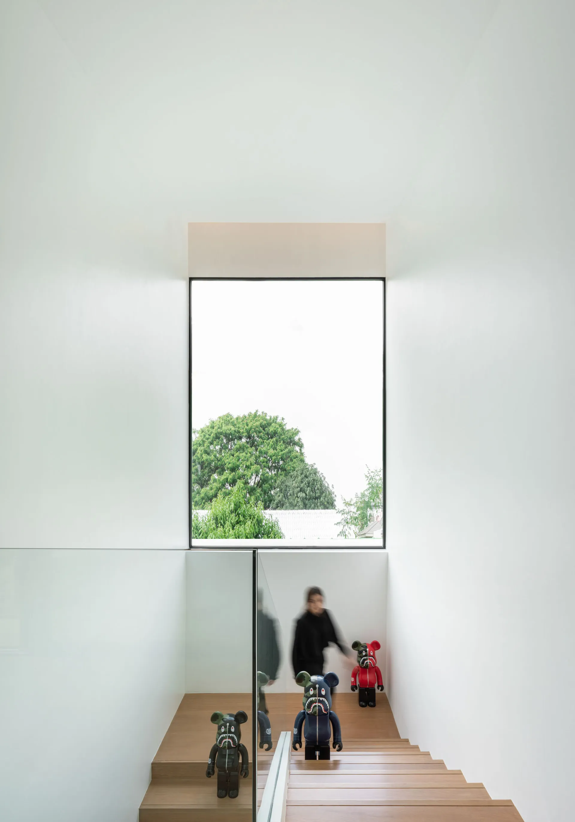 A minimalist staircase with wooden steps and glass railings, framed by a large window.