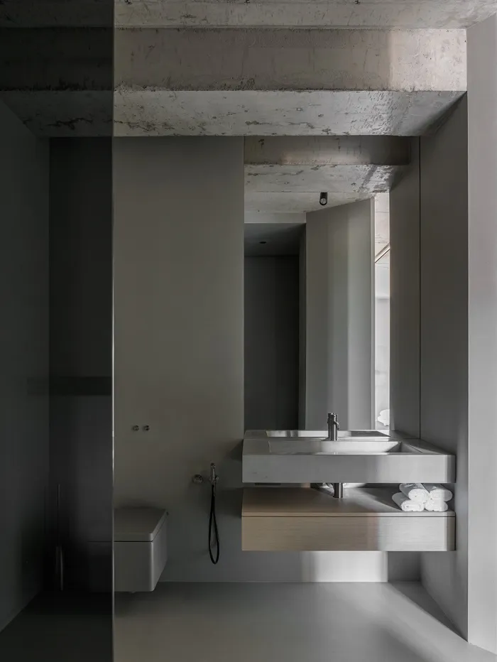 Modern minimalist bathroom with concrete walls and floor, featuring a floating sink with brushed metal fixtures and a towel s