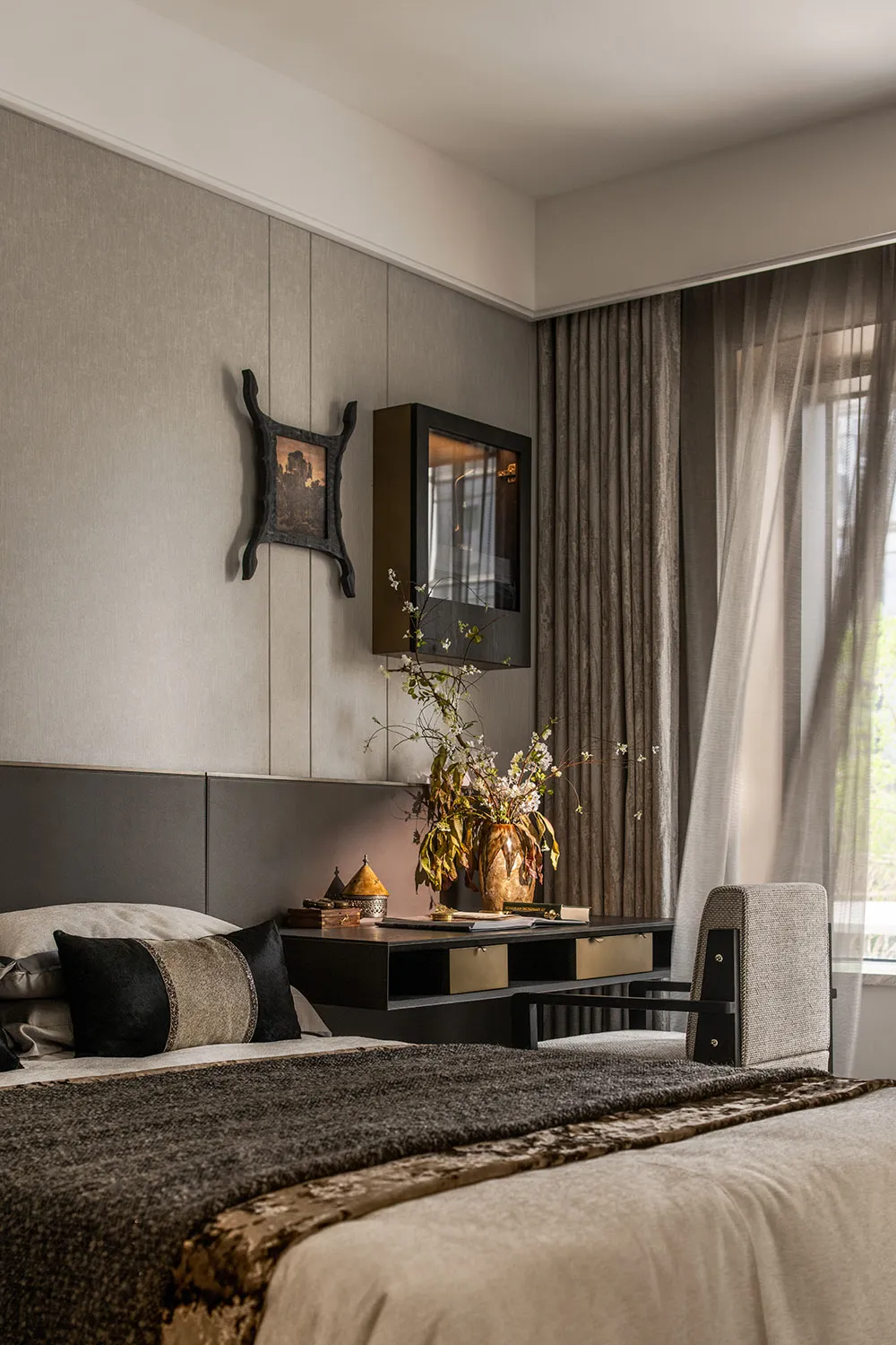 A modern bedroom featuring a bed with brown textiles, a side table with a vase of flowers, and a window with curtains.