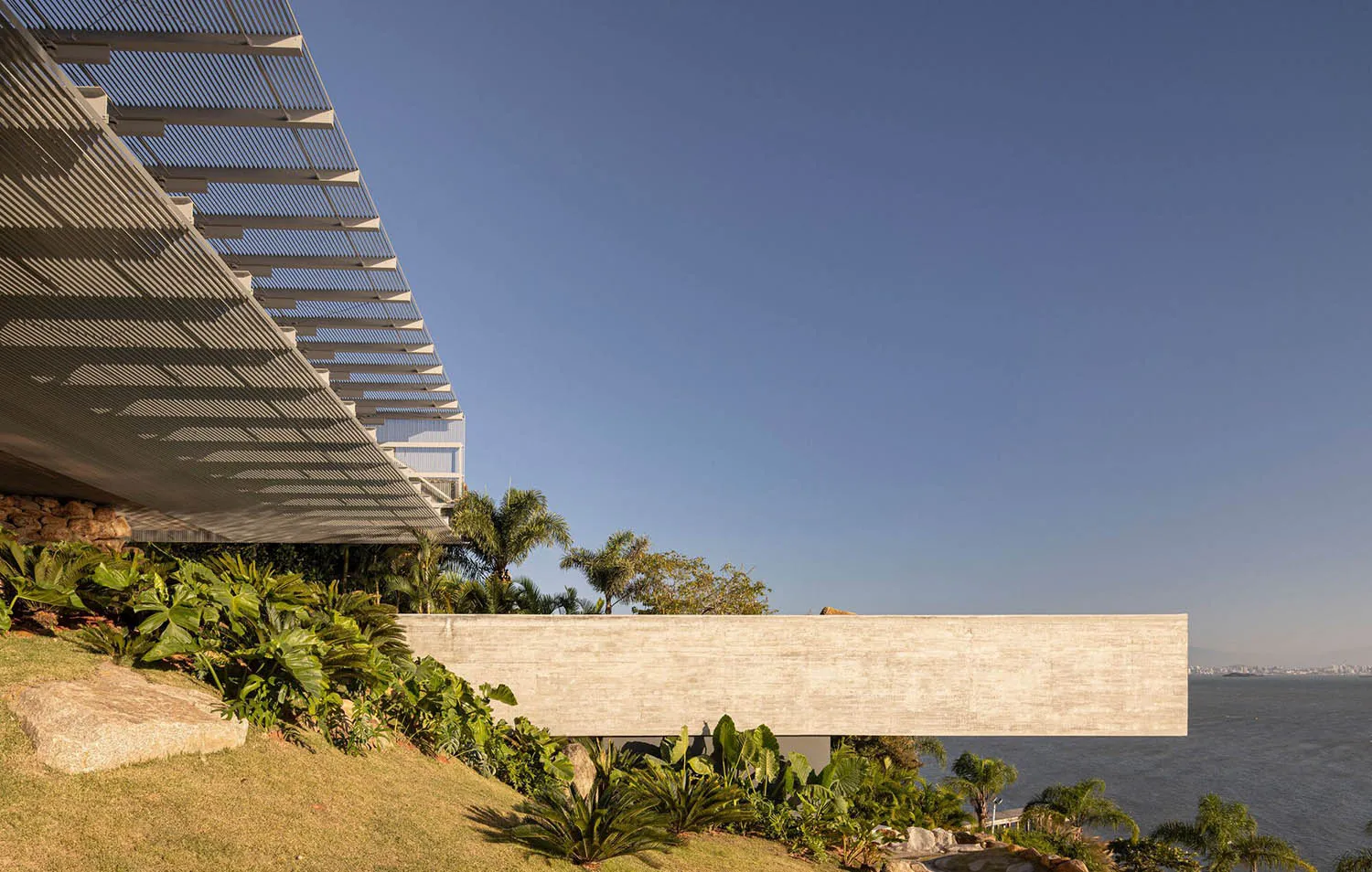 Modern building structure featuring exposed concrete with a garden and ocean view.
