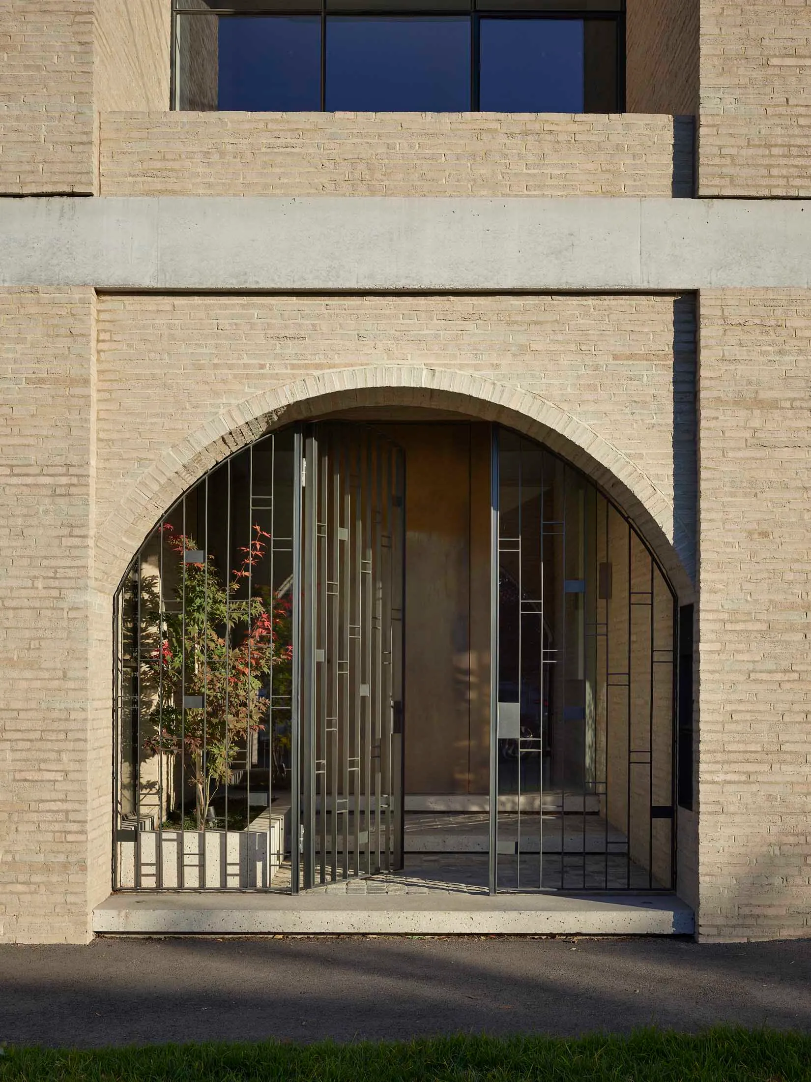 Modern entrance with an arched concrete gate and a glass door in the background.