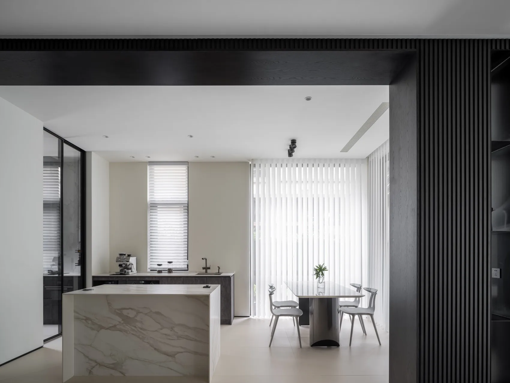 Modern minimalist kitchen featuring white marble countertops and a sleek dining area with vertical blinds.