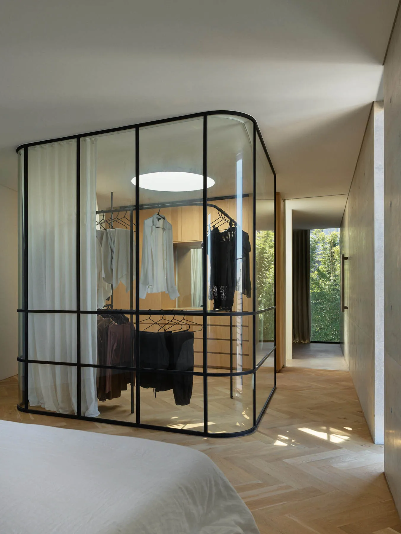 Modern minimalist closet with glass walls displaying hanging clothes.