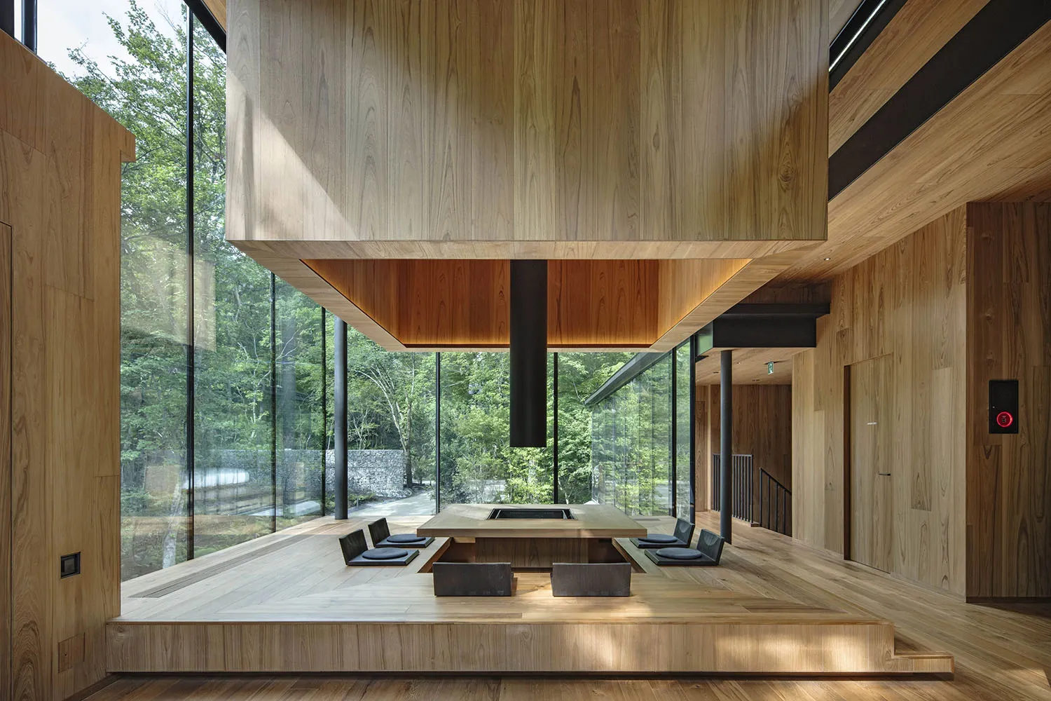 A modern wooden interior with an open-concept design, featuring a central fireplace and sliding glass doors overlooking a for