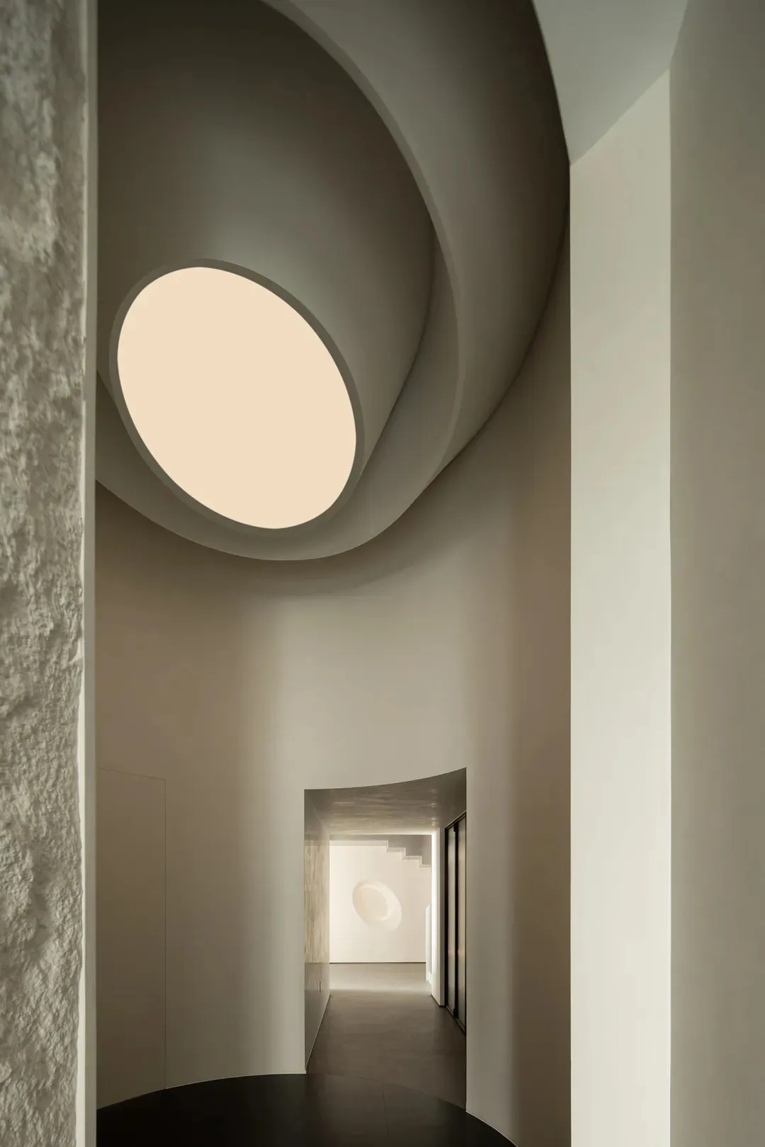 A minimalist interior with a concrete spiral staircase and a circular window letting in natural light.