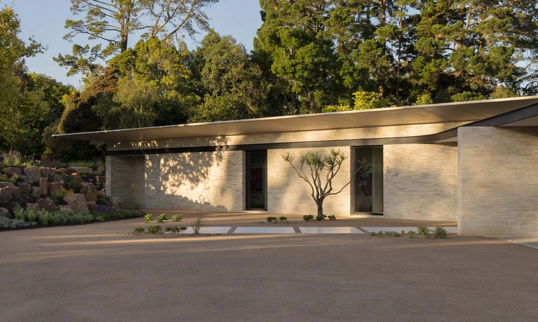A modern home featuring a sandstone exterior with large glass windows and a sloped roof.