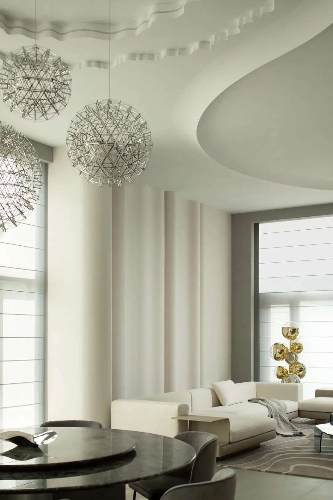A modern minimalist living room with white sofas, floor-to-ceiling windows, and metallic pendant lights hanging from the ceil