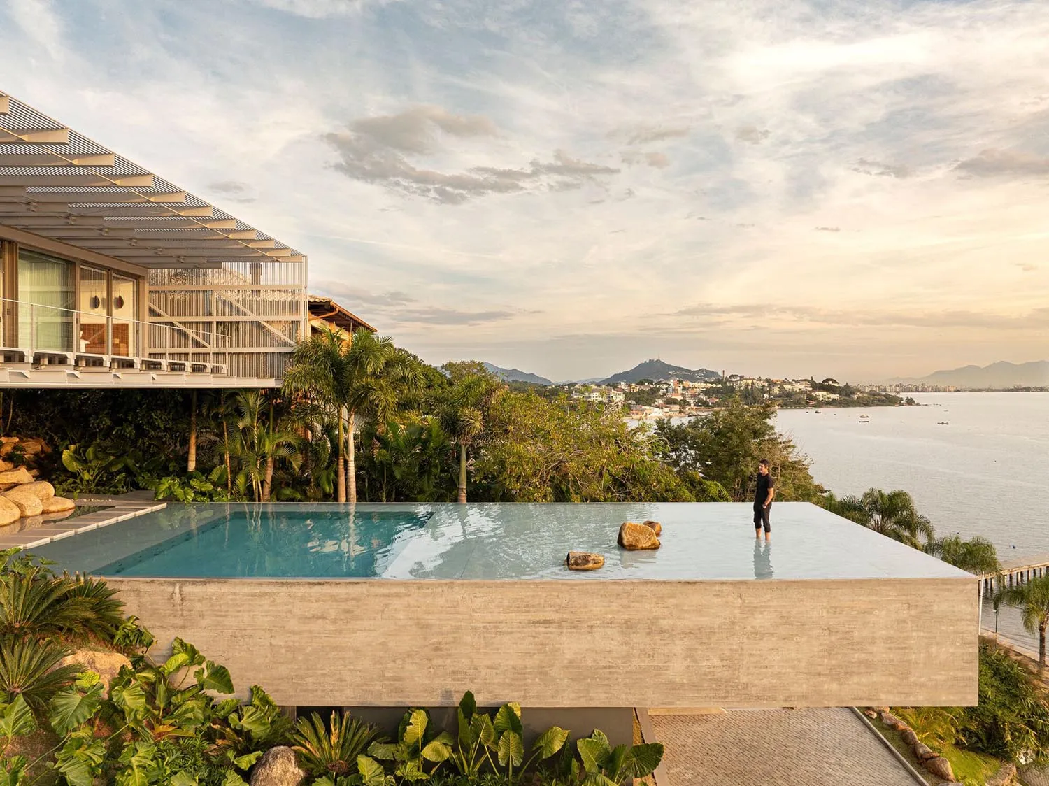 A modern residential exterior featuring a concrete structure with a rooftop pool overlooking the ocean and cityscape.
