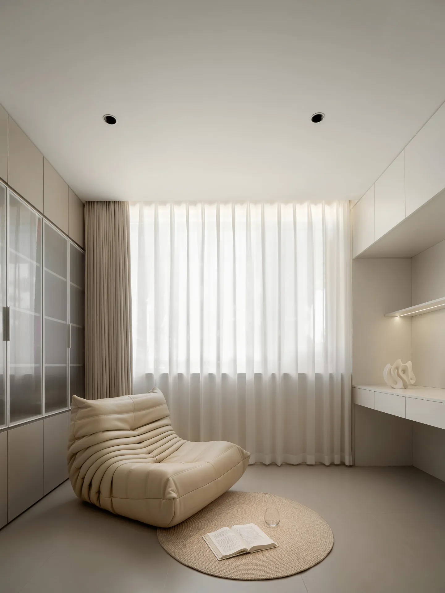 A serene bedroom with a beige armchair, an open book, and a glass of water on a round rug.