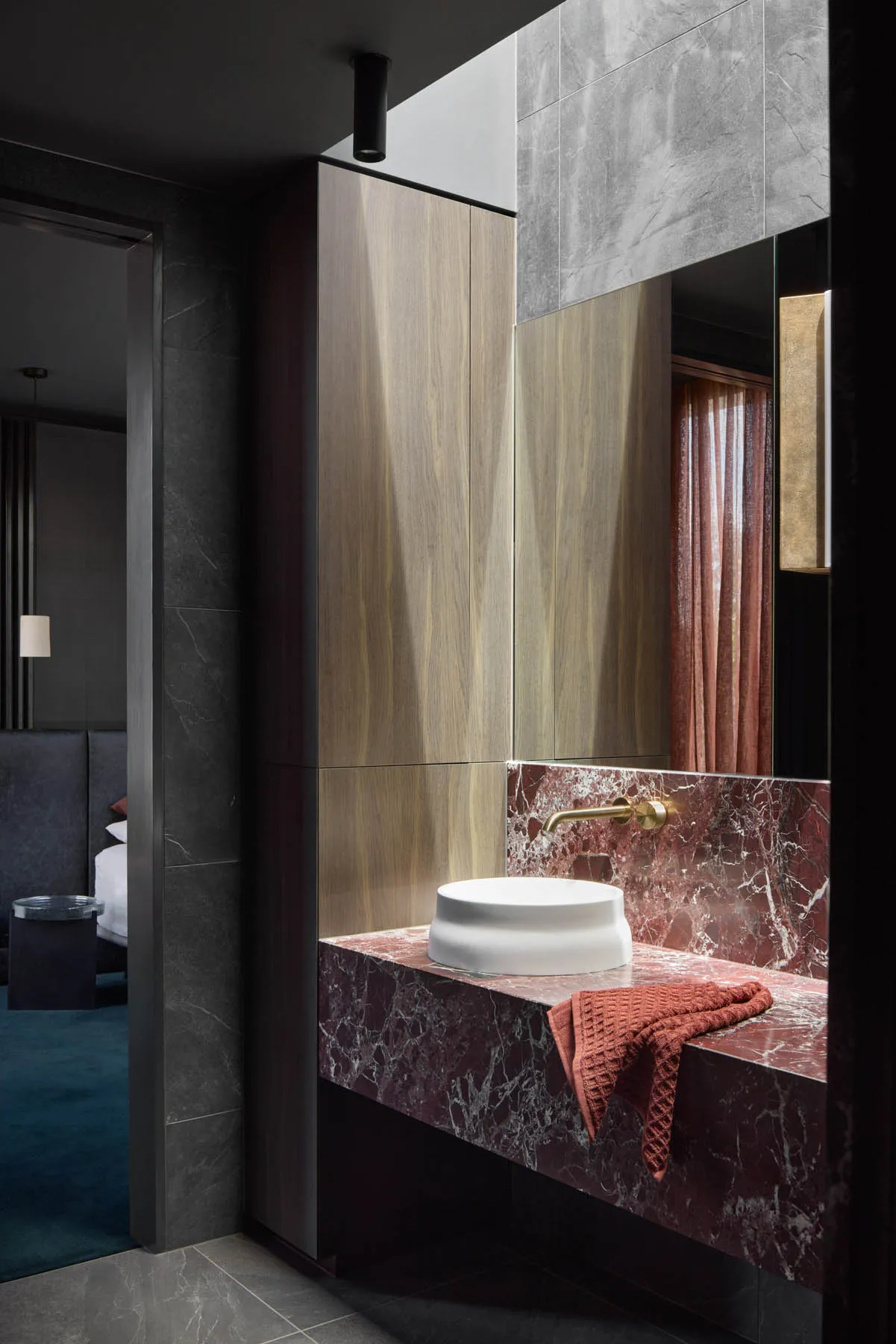 Modern minimalist bathroom featuring a white sink basin with a gold faucet, set against red marble and surrounded by sleek, d