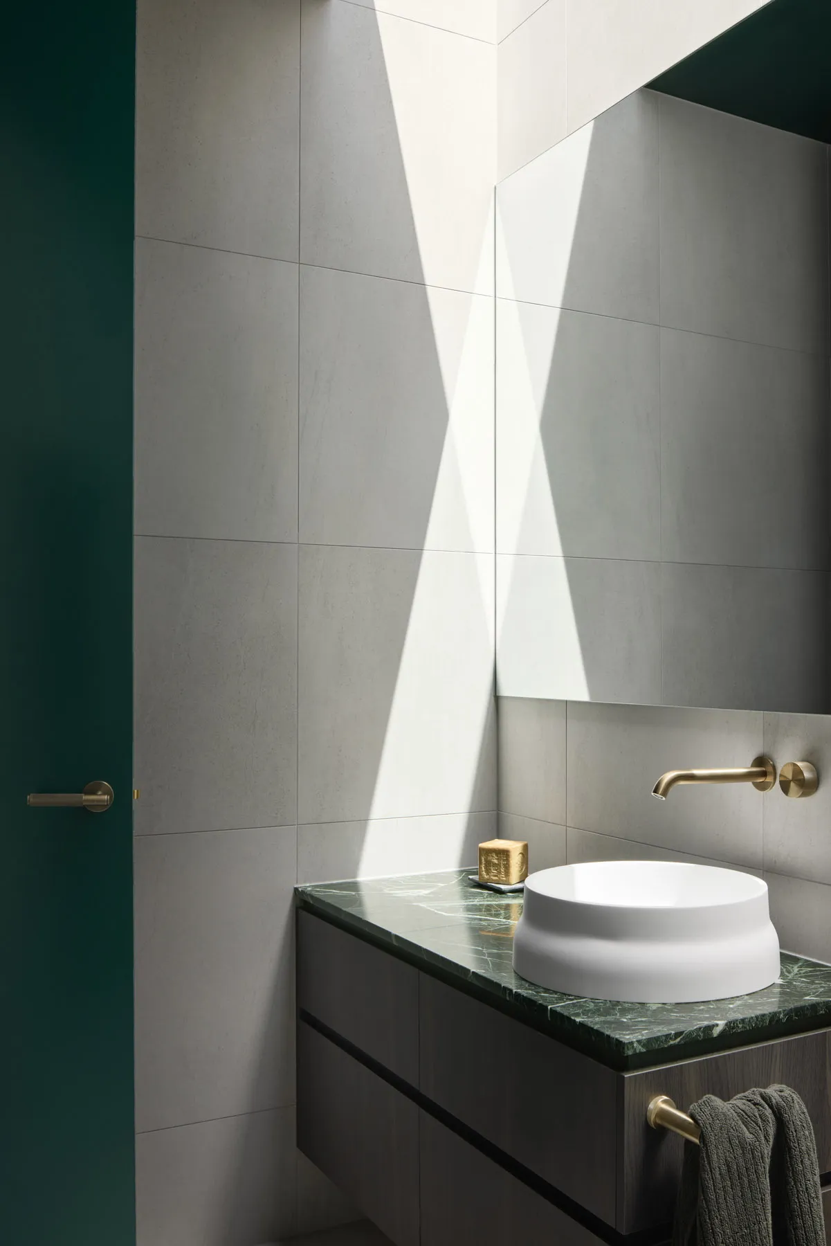 Modern bathroom with concrete walls and a round white sink on a green marble countertop.
