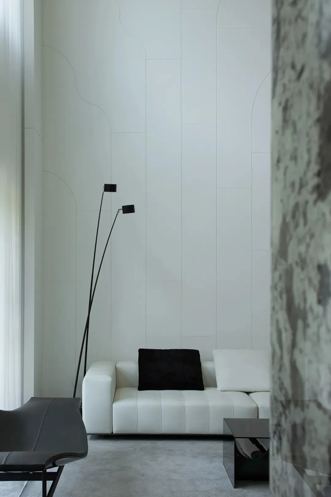 A minimalist living room featuring a white leather sofa with a black throw pillow, a marble side table, and a floor lamp with