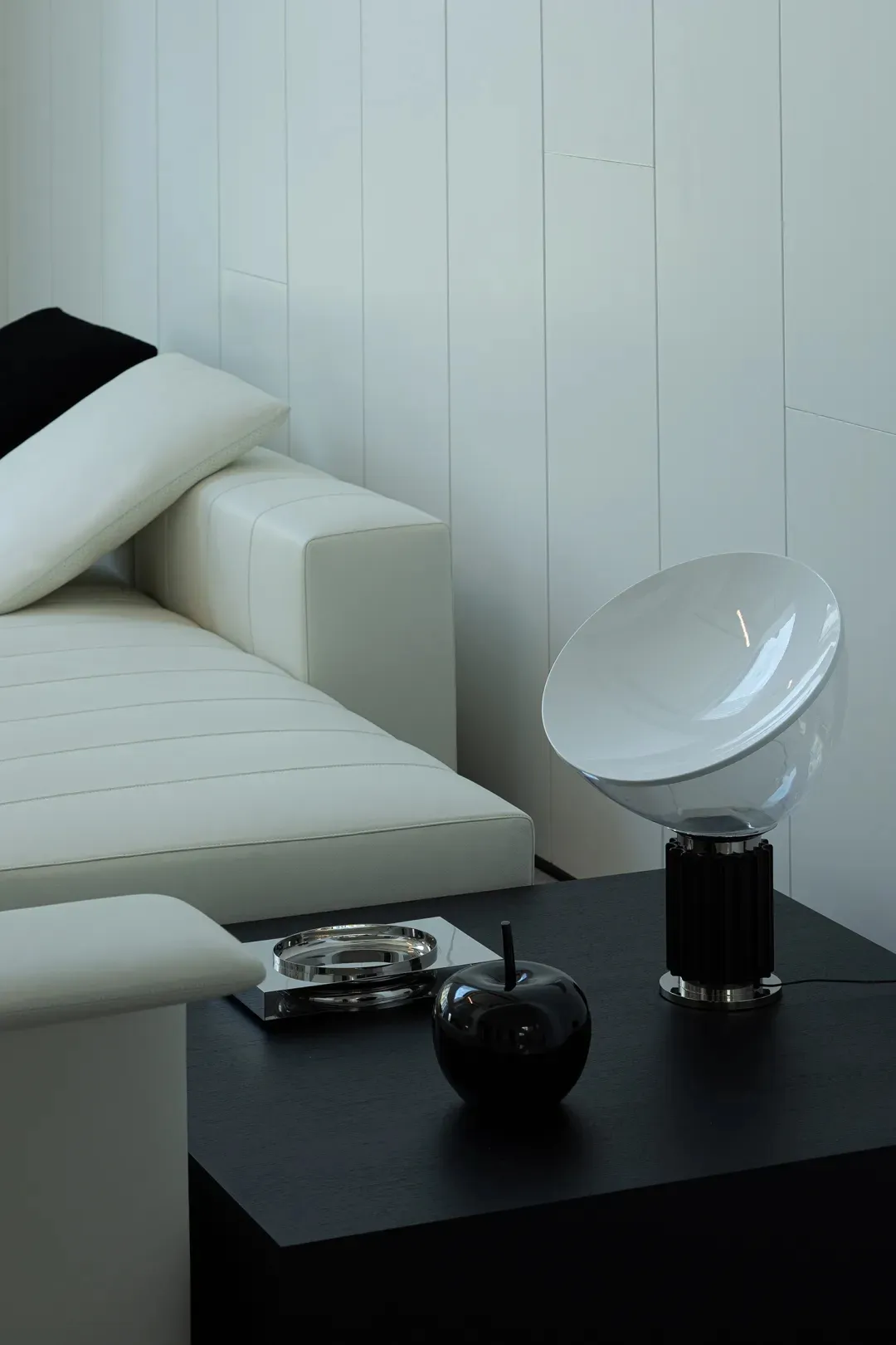 A modern interior design featuring a white leather sofa with black throw pillows, accompanied by a black and white table lamp
