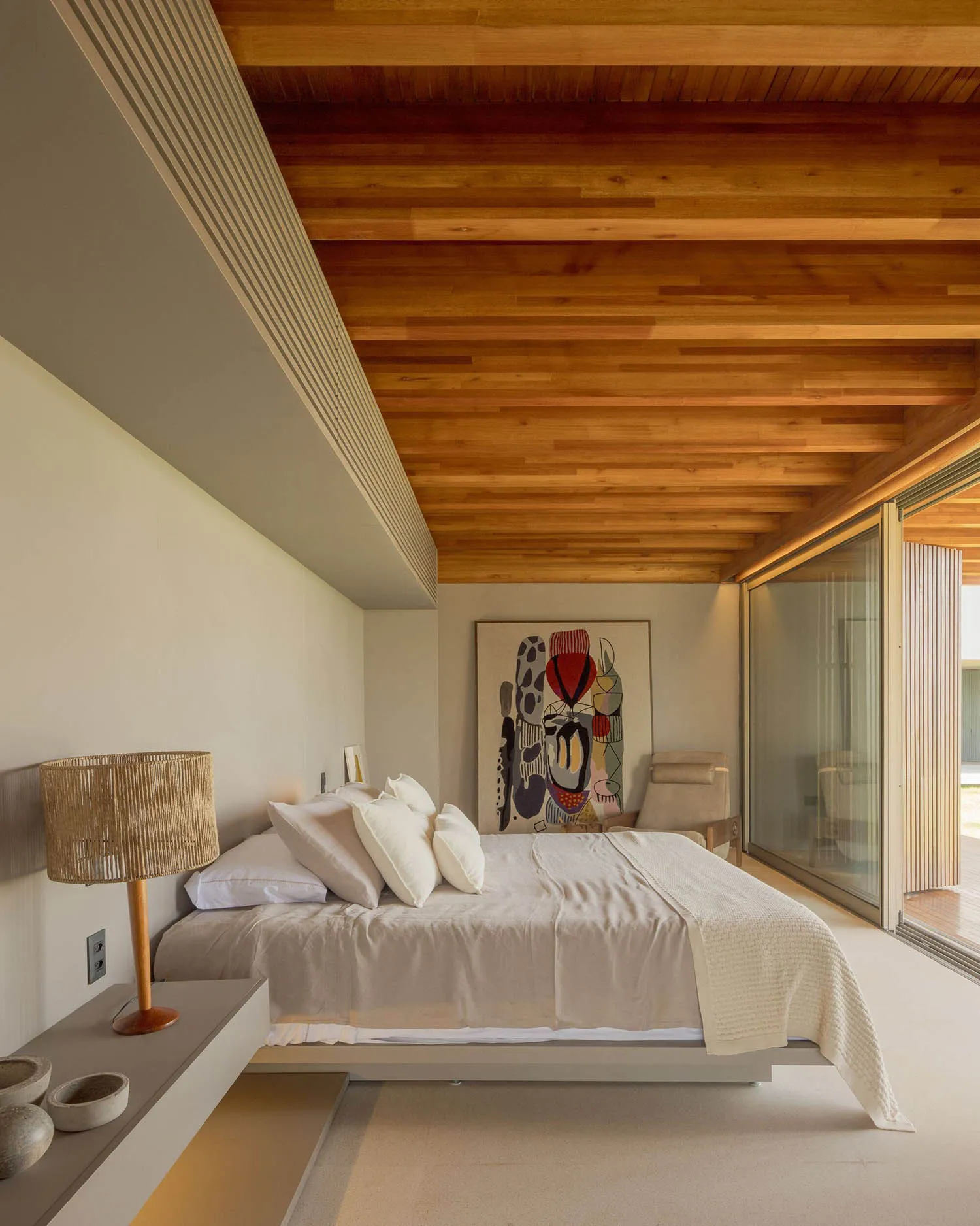 Neutral-toned modern minimalist bedroom with a wooden ceiling and a large abstract painting.