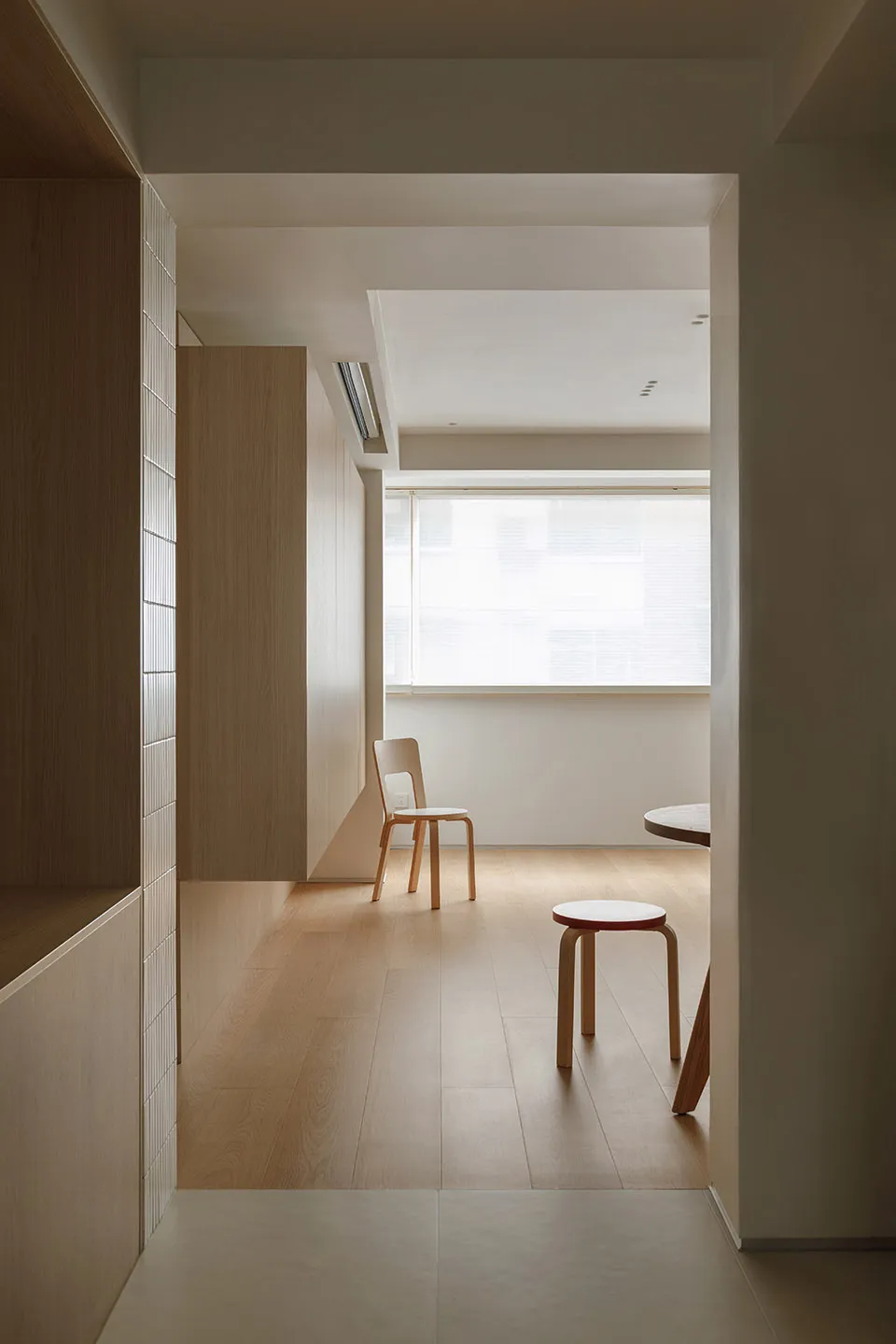 A minimalist living room featuring wooden flooring, a white chair, and a small table.