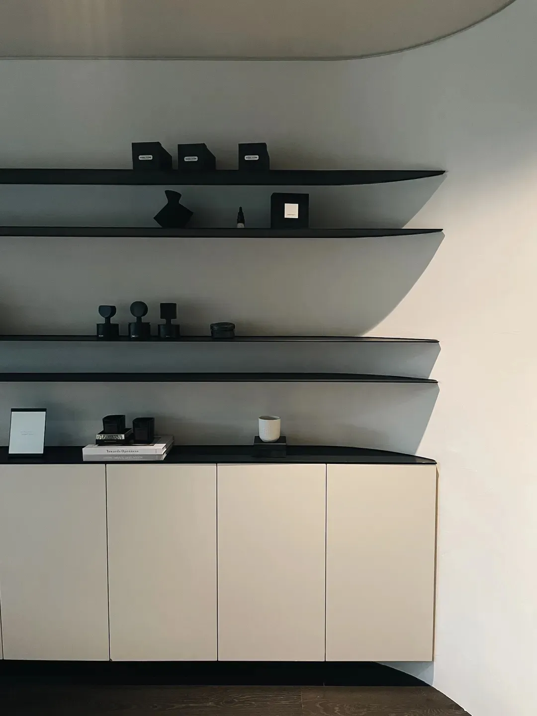 Modern minimalist interior with black glass shelves, white cream cabinets, and a concrete backdrop.