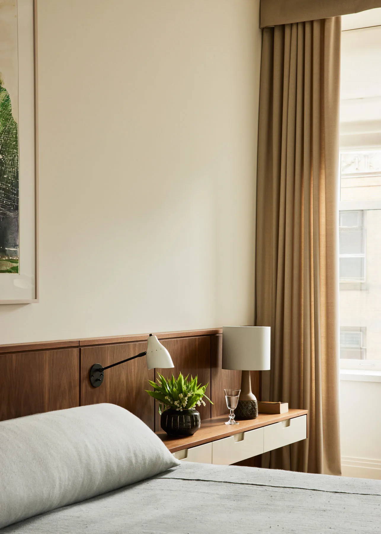 A modern bedroom with a wooden headboard, a bed with a light grey cover, and a nightstand with a white lamp and a green plant