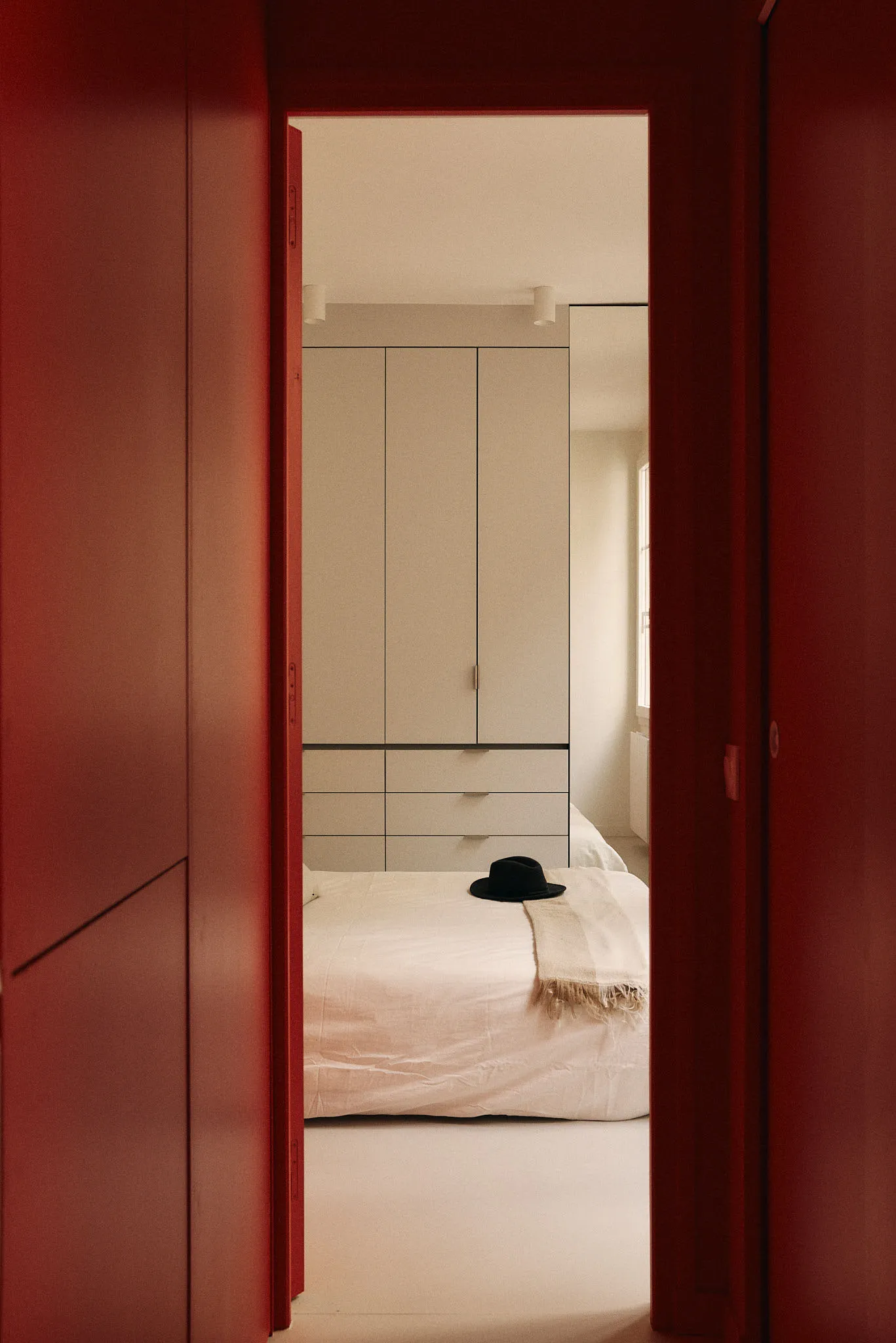 A minimalist bedroom with a white bed and a hat on it.