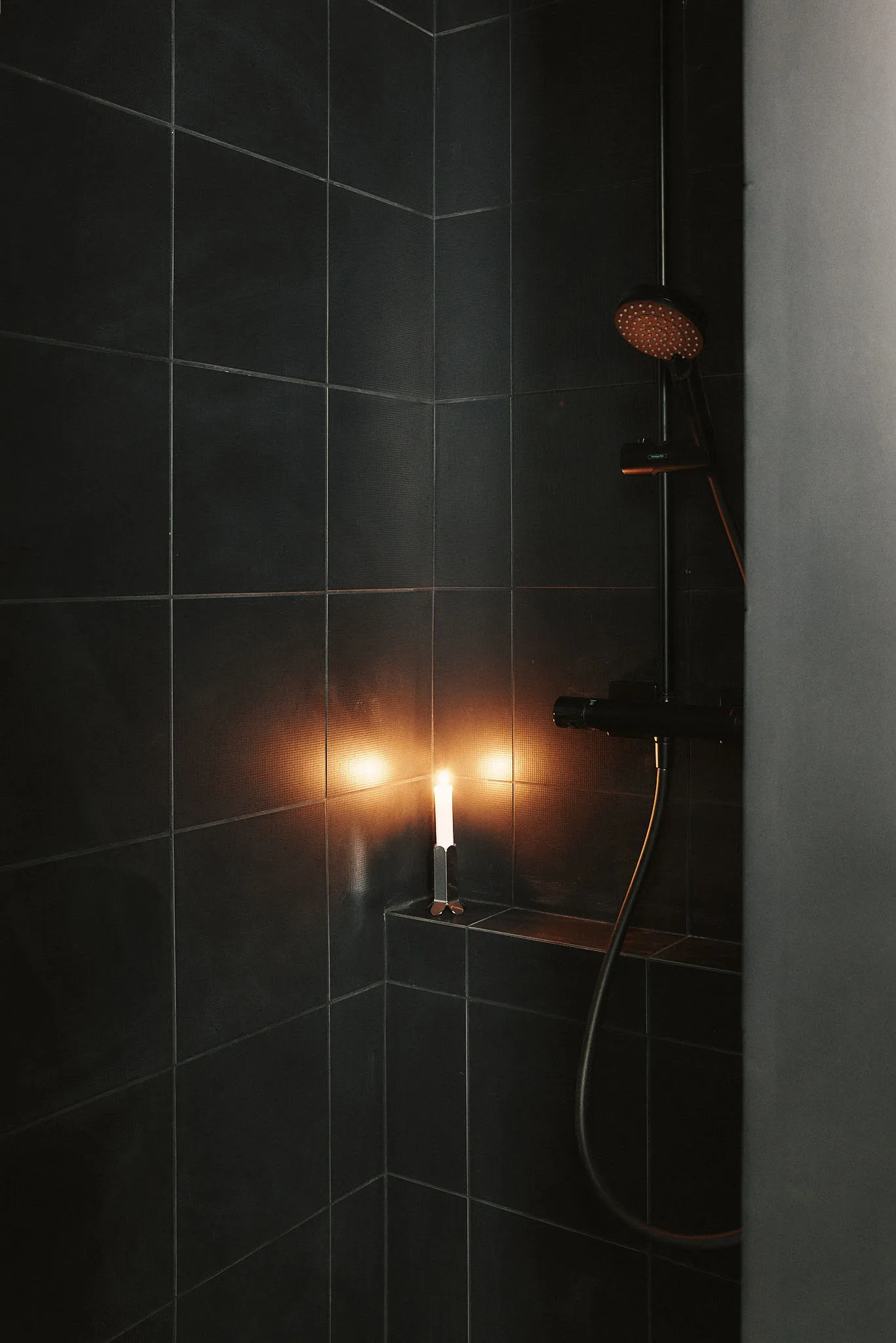 A minimalist bathroom with black tiles and a glowing candle.