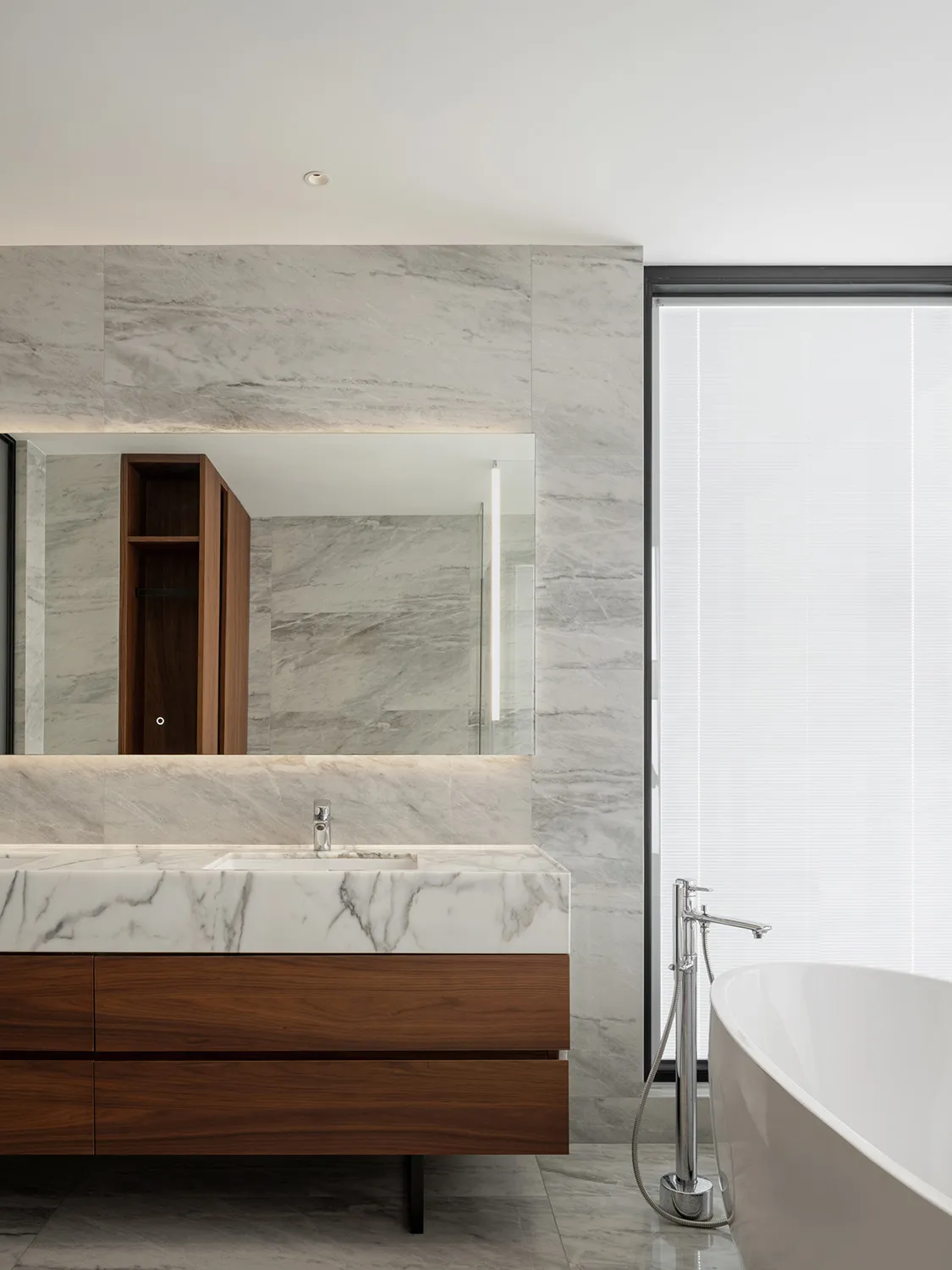 Modern bathroom featuring marble countertop and wood vanity with a freestanding bathtub and large window.