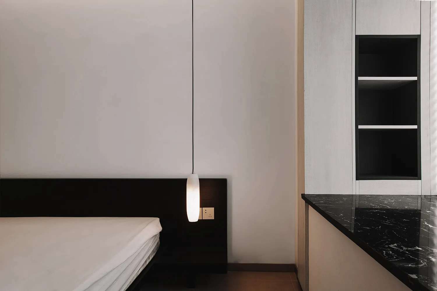 A minimalist bedroom featuring a bed with a simple black headboard, a sleek black light fixture, and a marble countertop.