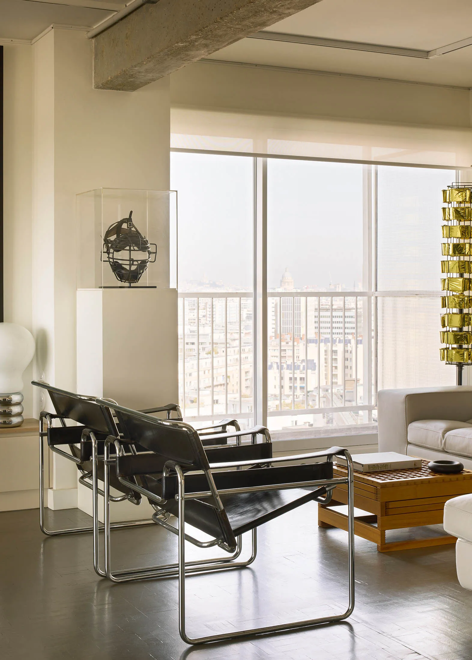 Modern minimalist living room featuring black leather chairs and metal frame, with a view of the cityscape through large wind