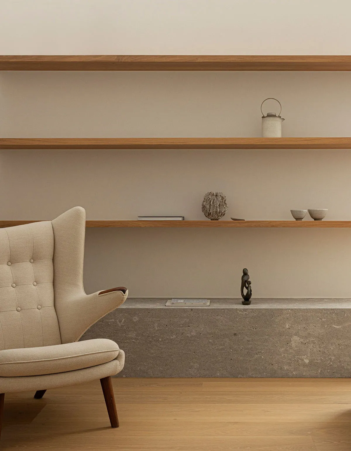 A minimalist living room with wooden concrete shelves, a beige upholstered armchair, and decorative objects.