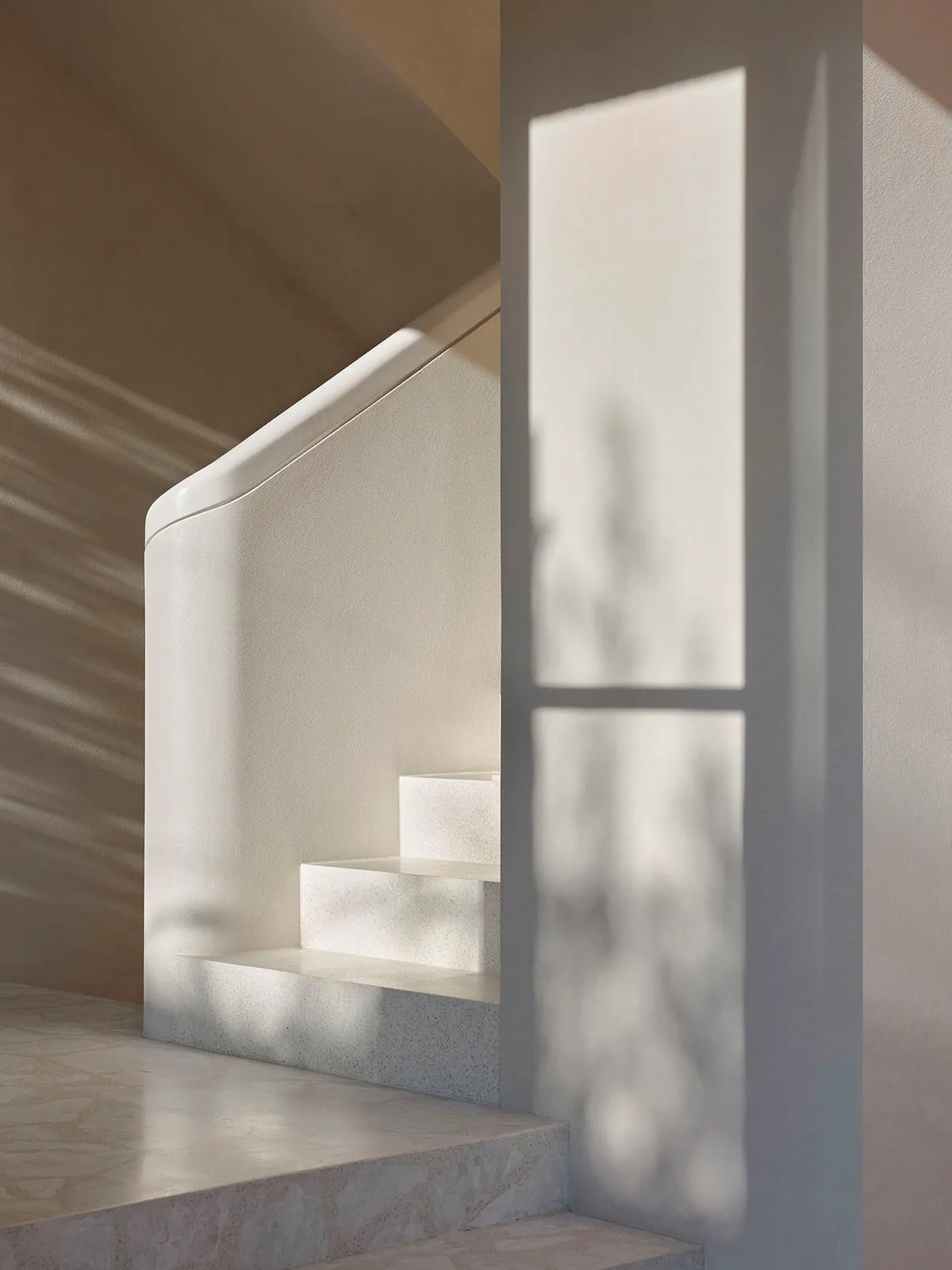 Modern staircase with marble steps and concrete wall, featuring light filtering through a window.