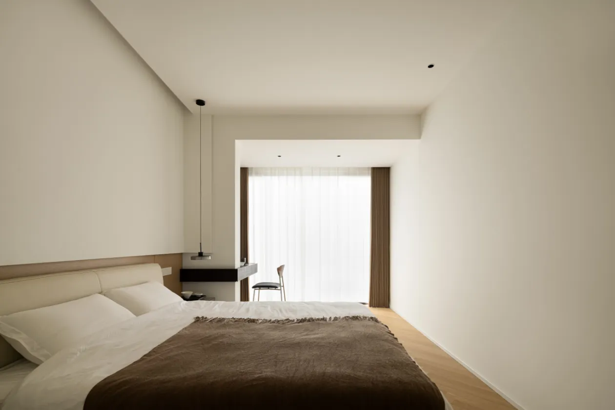 A minimalist bedroom with neutral-toned furniture, white bed linen, and a simple design.