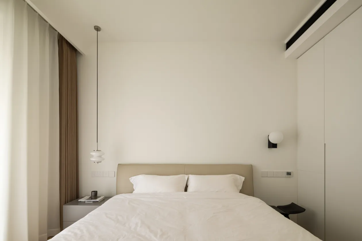 Modern minimalist bedroom with a bed, nightstand, and white walls.