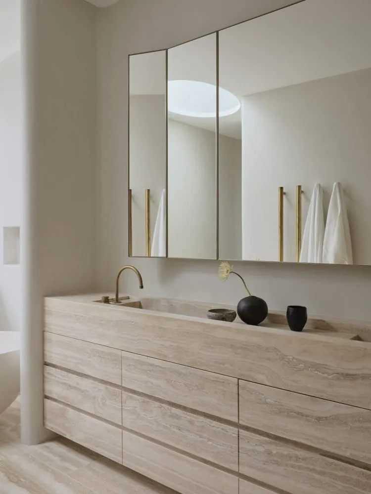 Modern minimalist bathroom with a stone countertop and sink, featuring a large mirror and brass accents.