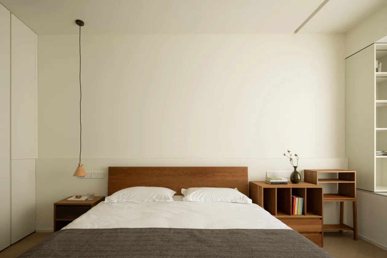 A minimalist bedroom featuring a wooden bed with white bedding and a pendant light hanging from the ceiling.