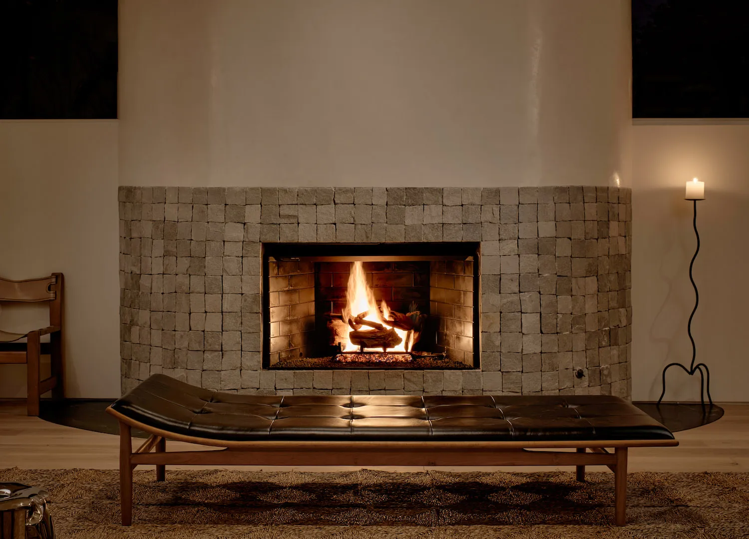 Minimalist living room with a stone fireplace, wood bench, and candle.