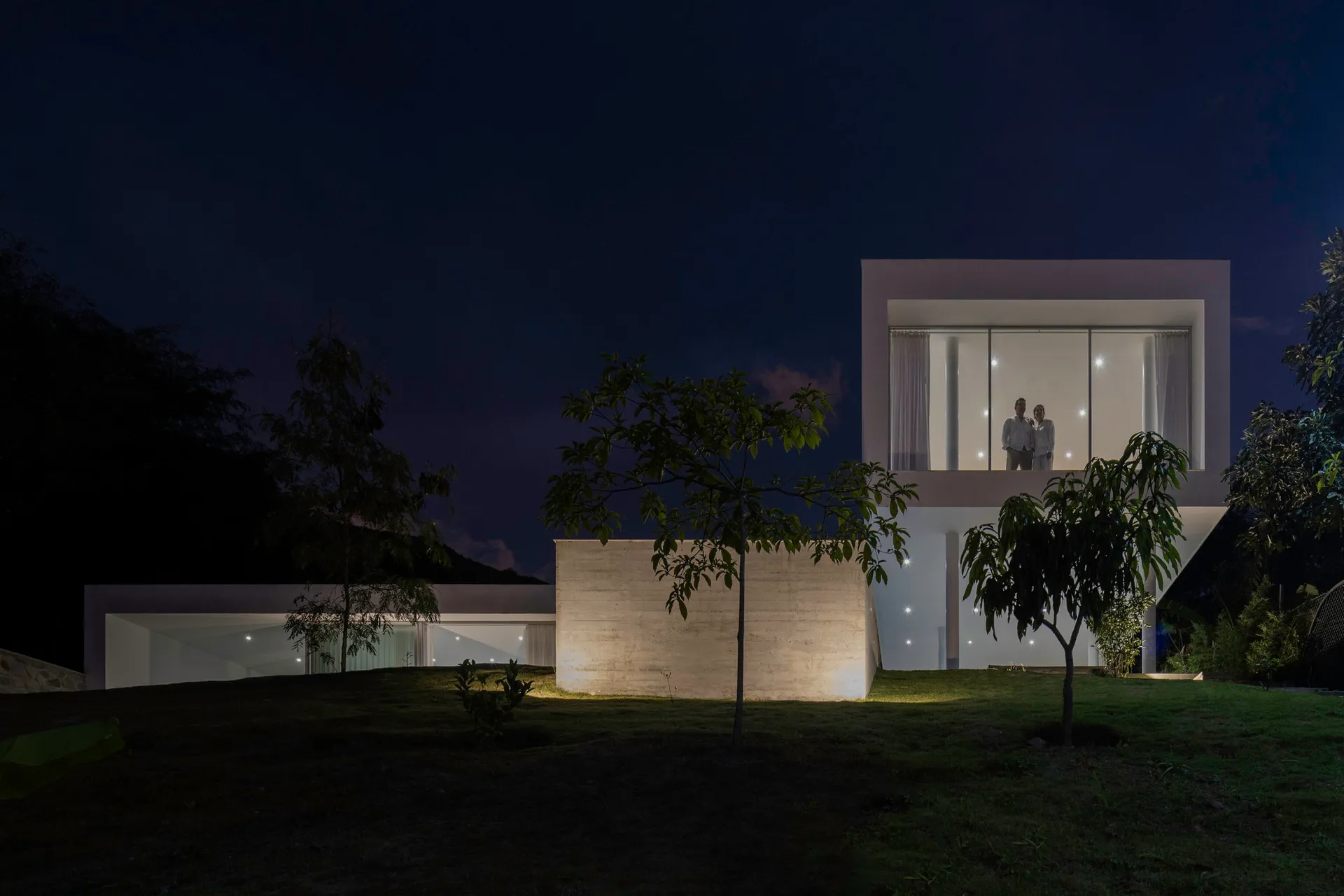夜晚的現代住宅建築,外牆為混凝土材質並搭配大型窗戶。