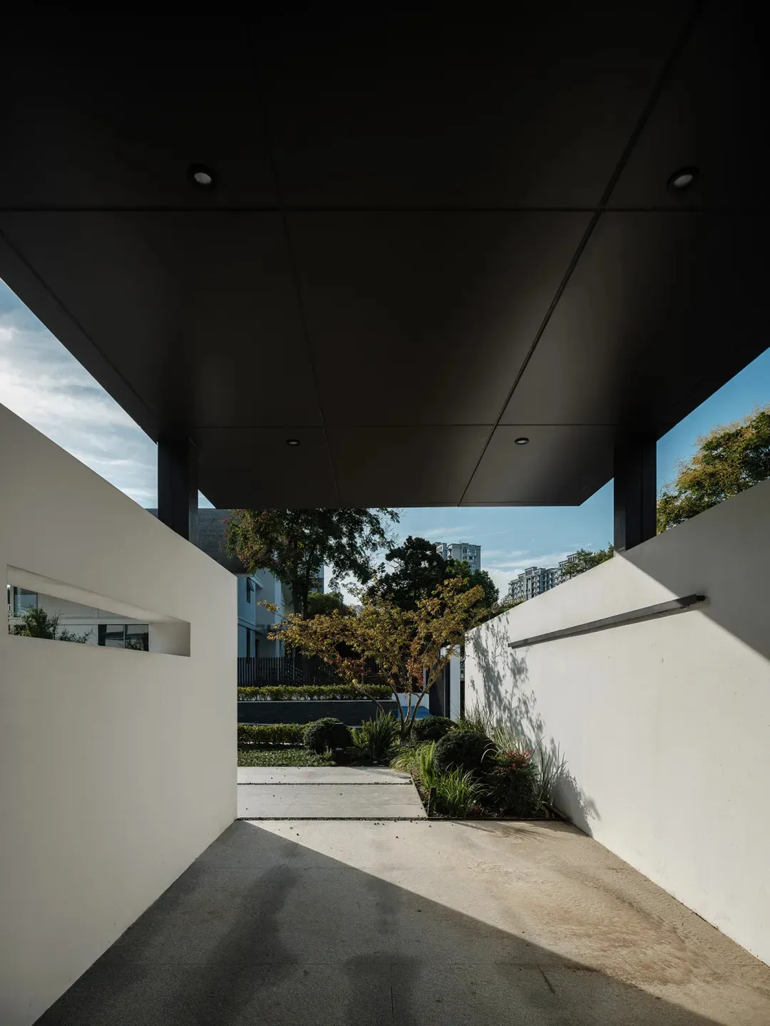 A modern entryway with concrete flooring, glass walls, and lush greenery and trees.