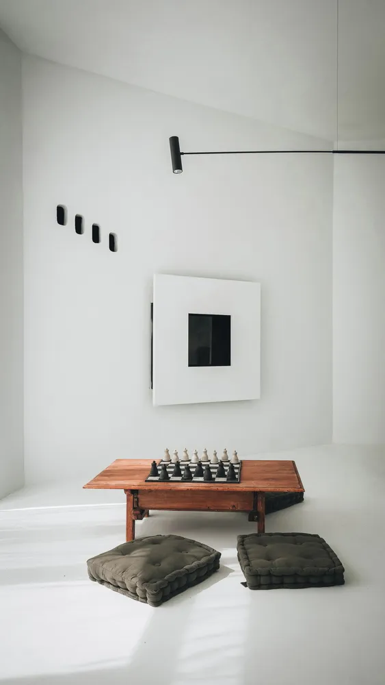 極簡風格的客廳空間,擺放木製桌椅、國際象棋棋子、綠色抱枕、黑色壁燈以及白色牆面