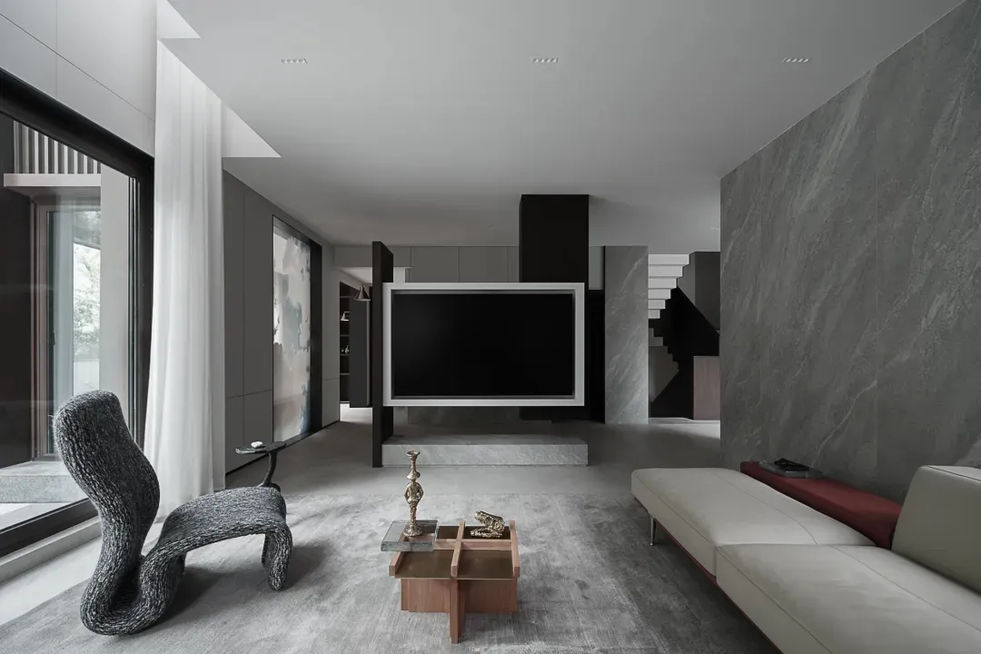 A modern living room featuring concrete walls and flooring, minimalist furniture, and a large window.