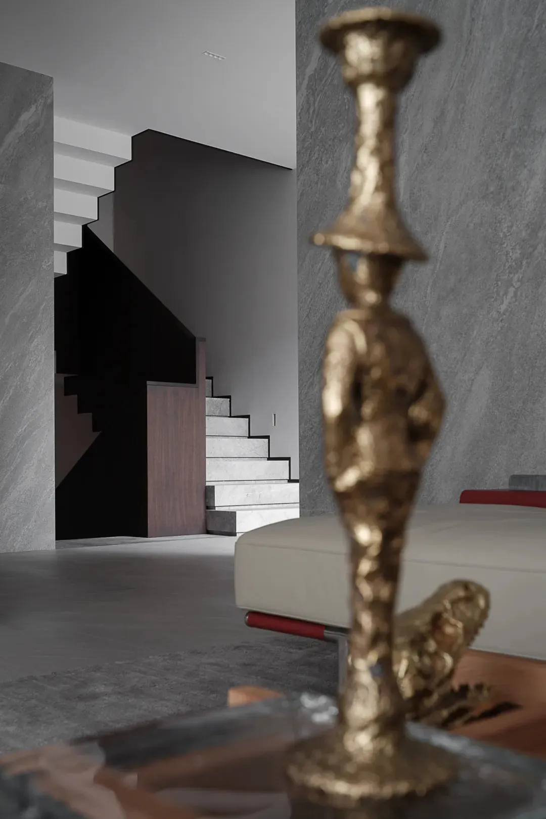 Modern interior space featuring a metallic statue on a shelf, with a staircase in the background.