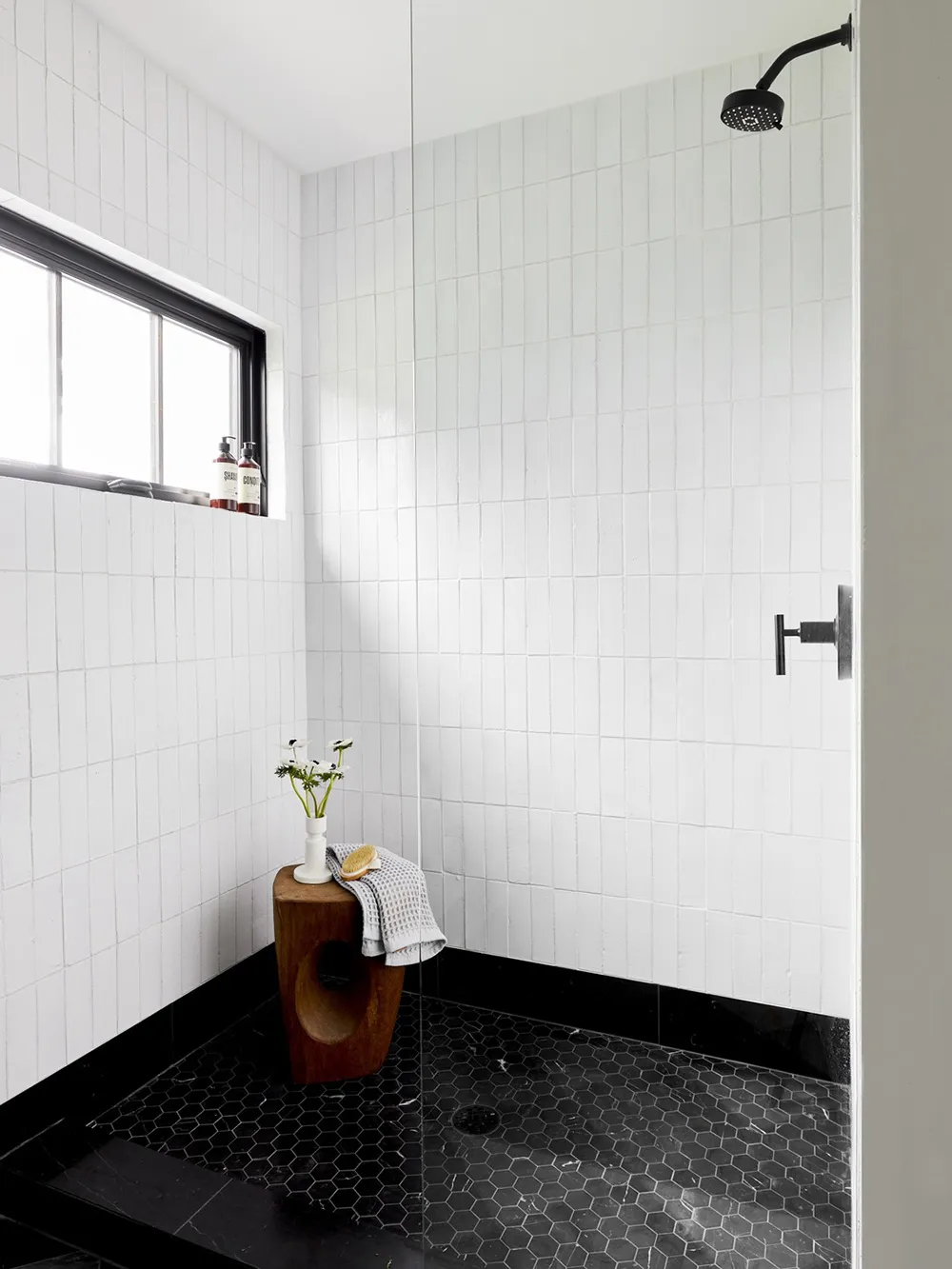 A modern bathroom with white tiled walls and black hexagonal floor tiles, featuring a shower stall.