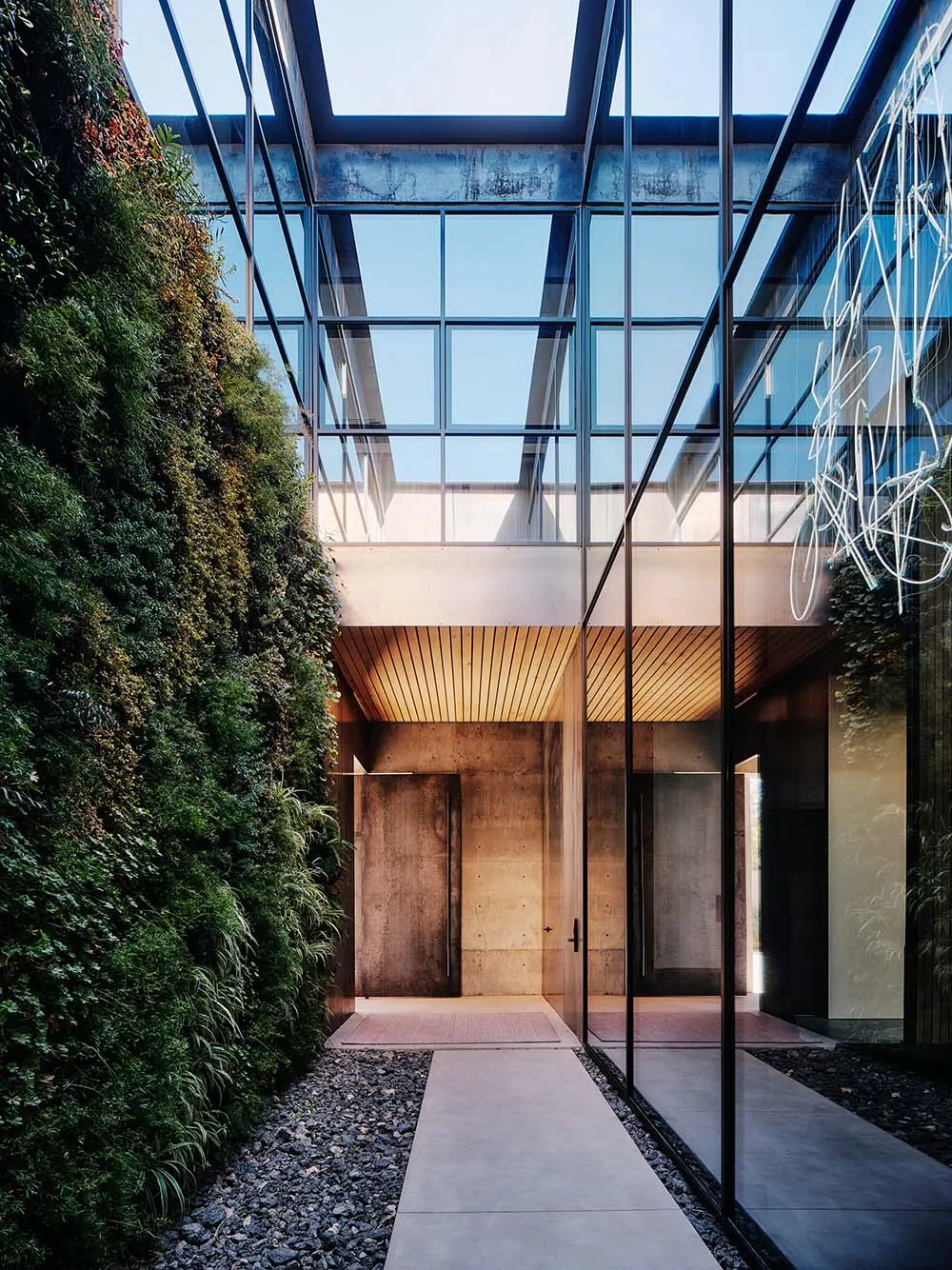 Modern industrial-style entranceway with concrete walls and a glass ceiling, featuring a green living wall on one side.