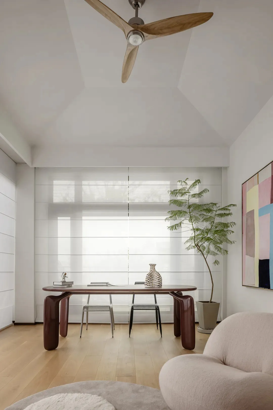 A modern minimalist office space featuring wooden furniture and a glass window with white blinds.